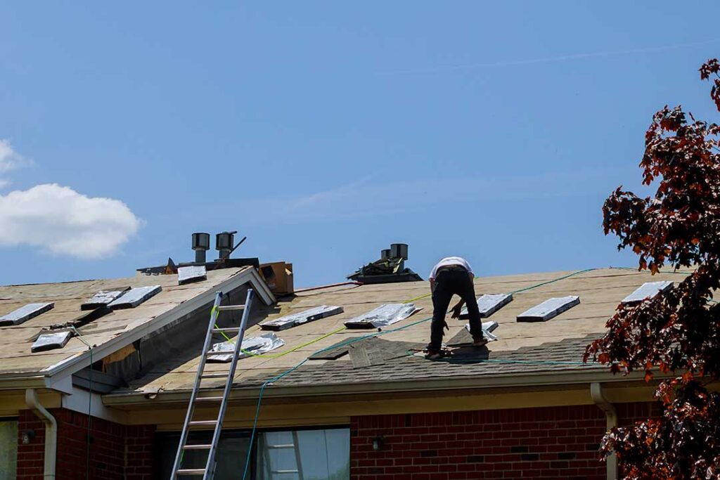Homeowner inspecting damaged shingles from the ground after a storm.