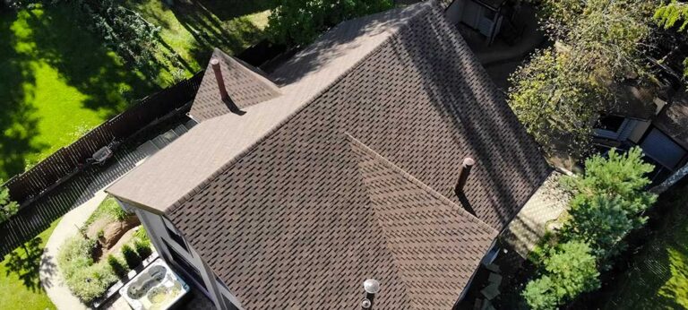Homeowner reviews roof damage photos and insurance papers at a kitchen table after a storm.